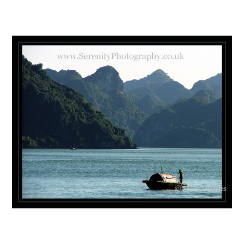 Small covered boat floats between the Islands of Halong Bay, Vietnam.